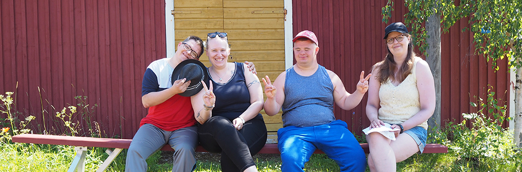 Personer med Downs syndrom sitter på en bänk tillsammans med två kvinnor.