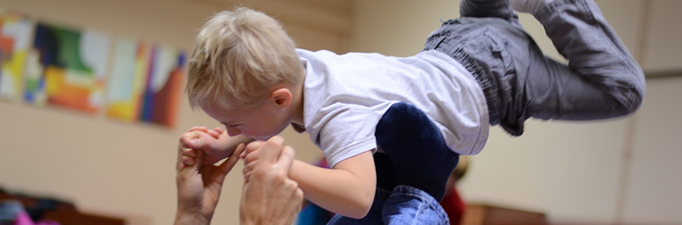 Pojke håller i sin pappas händer och flyger på hans ben