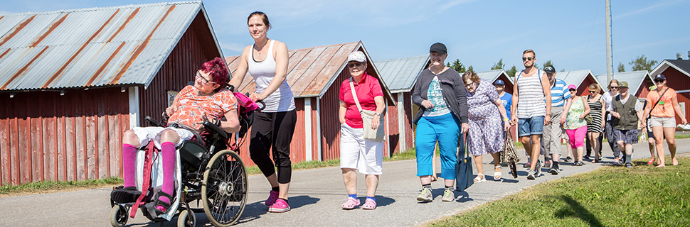 Personer med funktionsnedsättning och personal på promenad i somrig miljö.