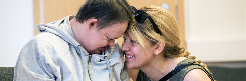 Kvinna på knä mot en kvinna med funktionsnedsättning, tittar varandra ömt i ögonen.