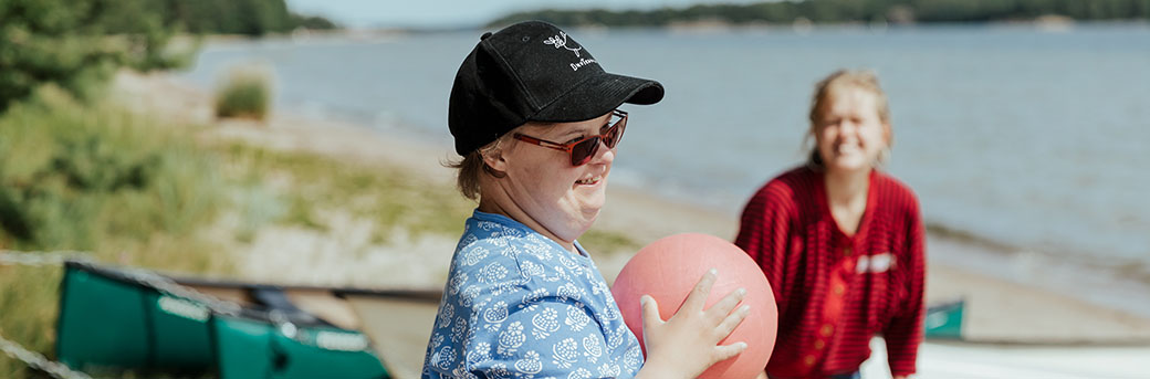 Personer med Downs syndrom håller på att kasta en boll till en kvinna på en sandstrand.