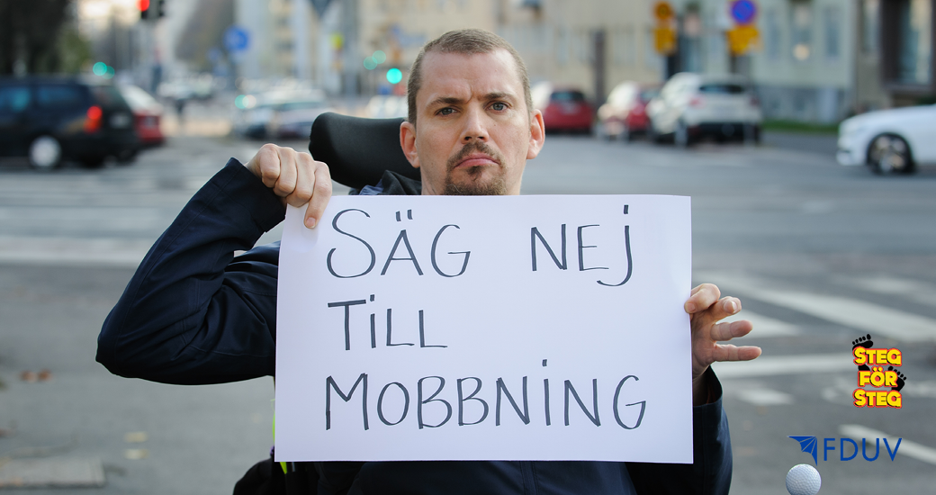 Man i rullstol håller upp ett papper med texten Säg nej till mobbning.
