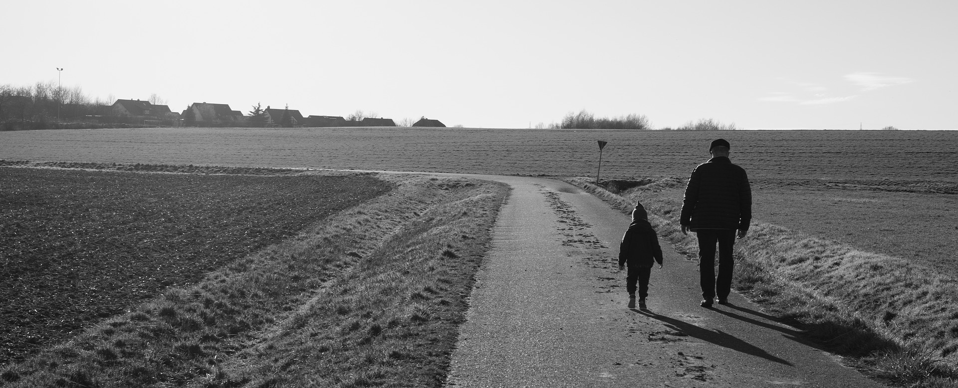 Himmel och ängsmark med väg där en äldre man går med ett barn.