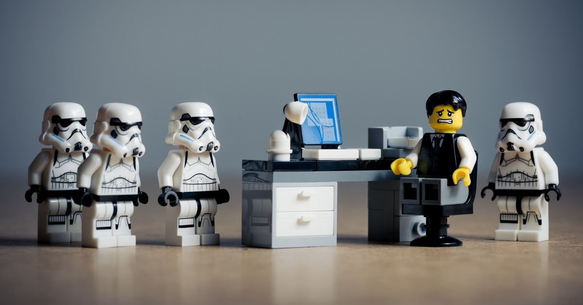 En bild som visar en legofigur som sitter vid ett skrivbord. Bredvid legofiguren står det legofigurer som föreställer storm trooper.