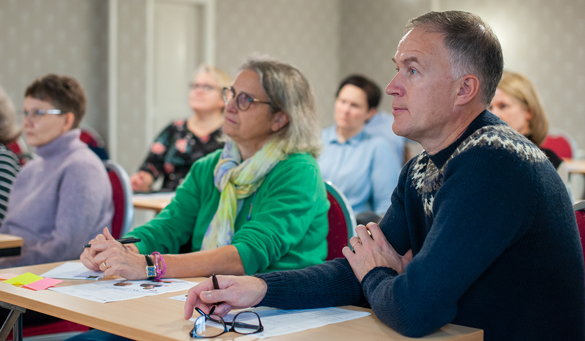 Personer vid bord följer med föreläsning.