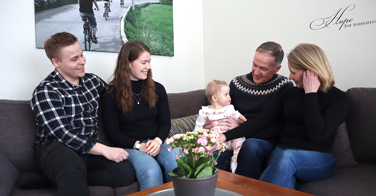 Familjen Mård och familjen Byggmäster sitter tillsammans i soffan och tittar på lilla Saga.