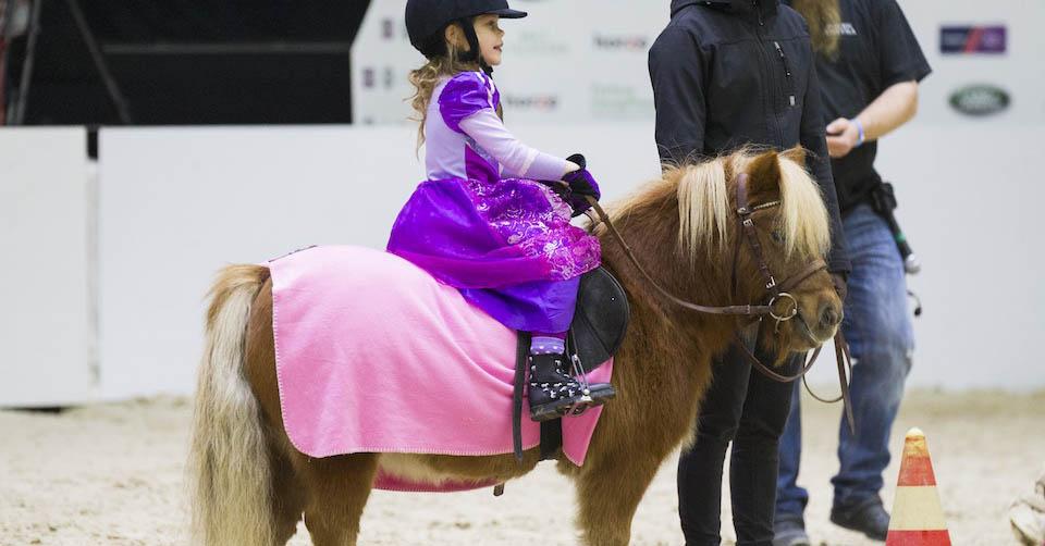 Flicka i prinsessklänning rider på en ponny.