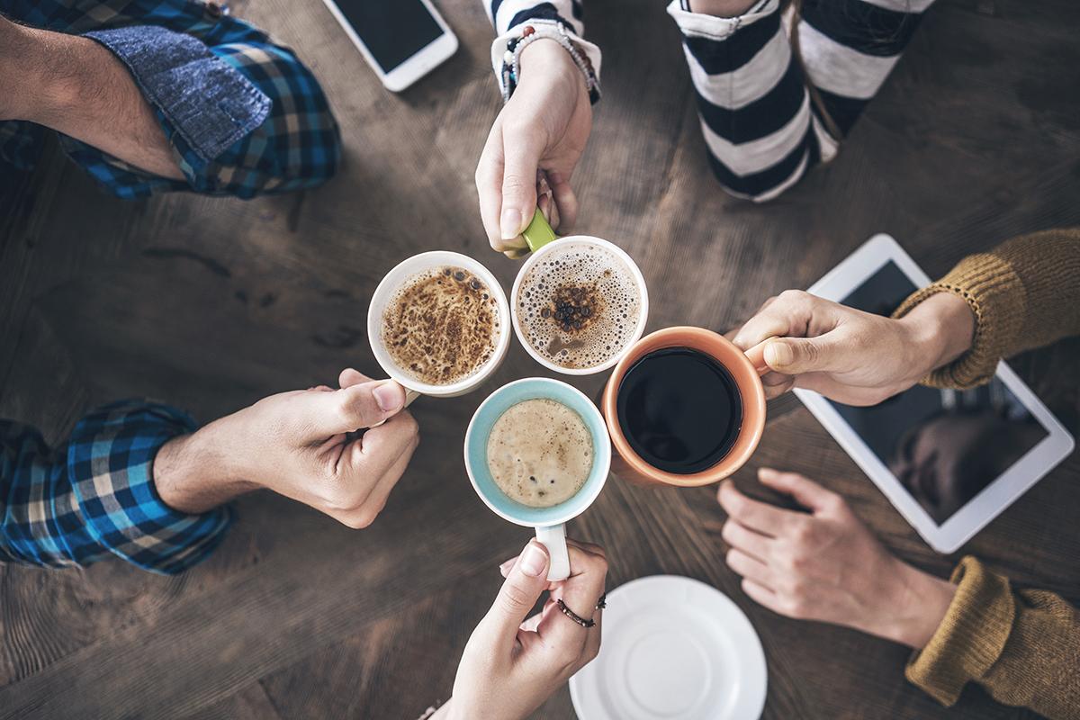 Händer som skålar i kaffekoppar samt mobiltelefoner.