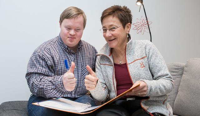 Man med Downs syndrom tittar tillsammans med kvinna i mapp, visar tummen upp.