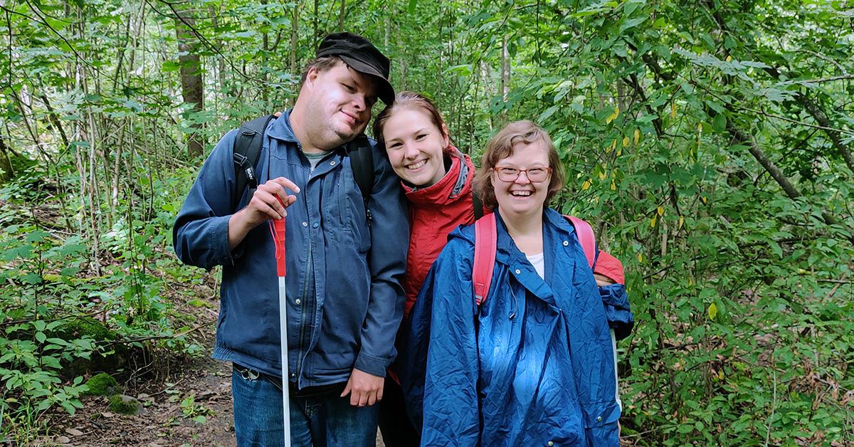 Tre personer håller om varandra och poserar i skogen.