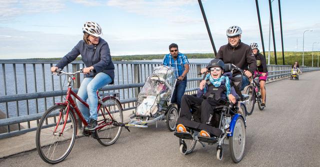Personer med funktionsnedsättning och andra tar sig över en bro med specialcyklar. 