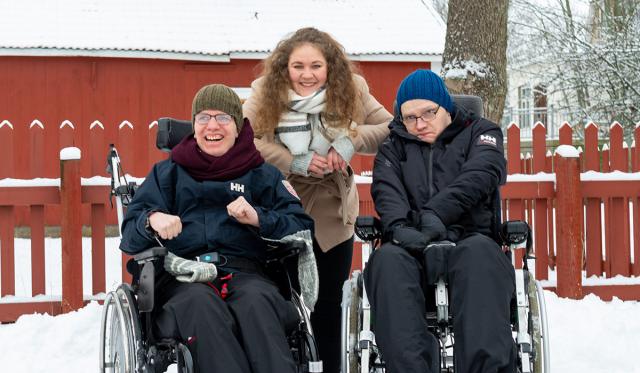 En kvinna mellan två män som sitter i rullstol.