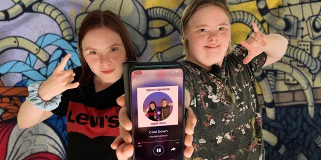 Två unga kvinnor visar en telefon med en bild av sången de just gjort