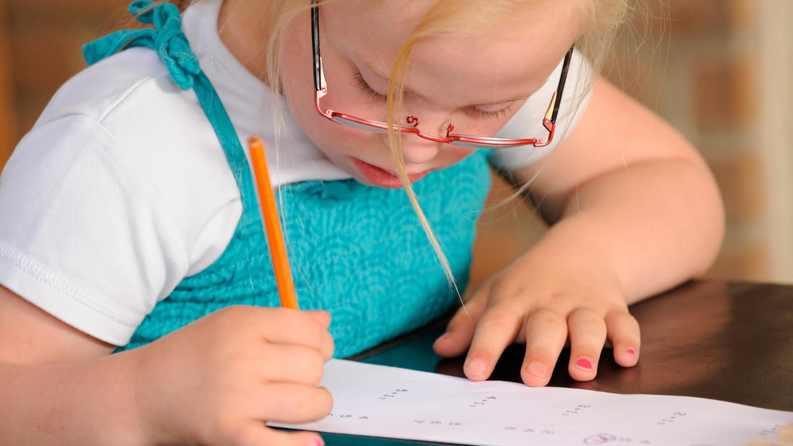 En flicka i skolåldern sitter vid ett bord och skriver.