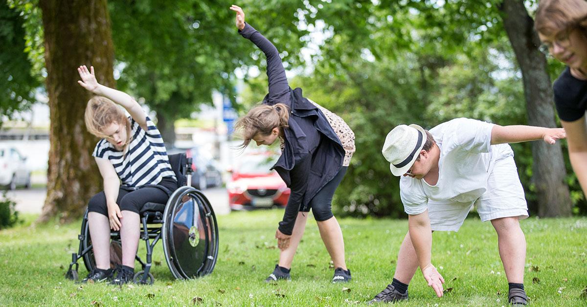 Tre personer varav en i rullstol gymnasiteserar i somrig miljö.