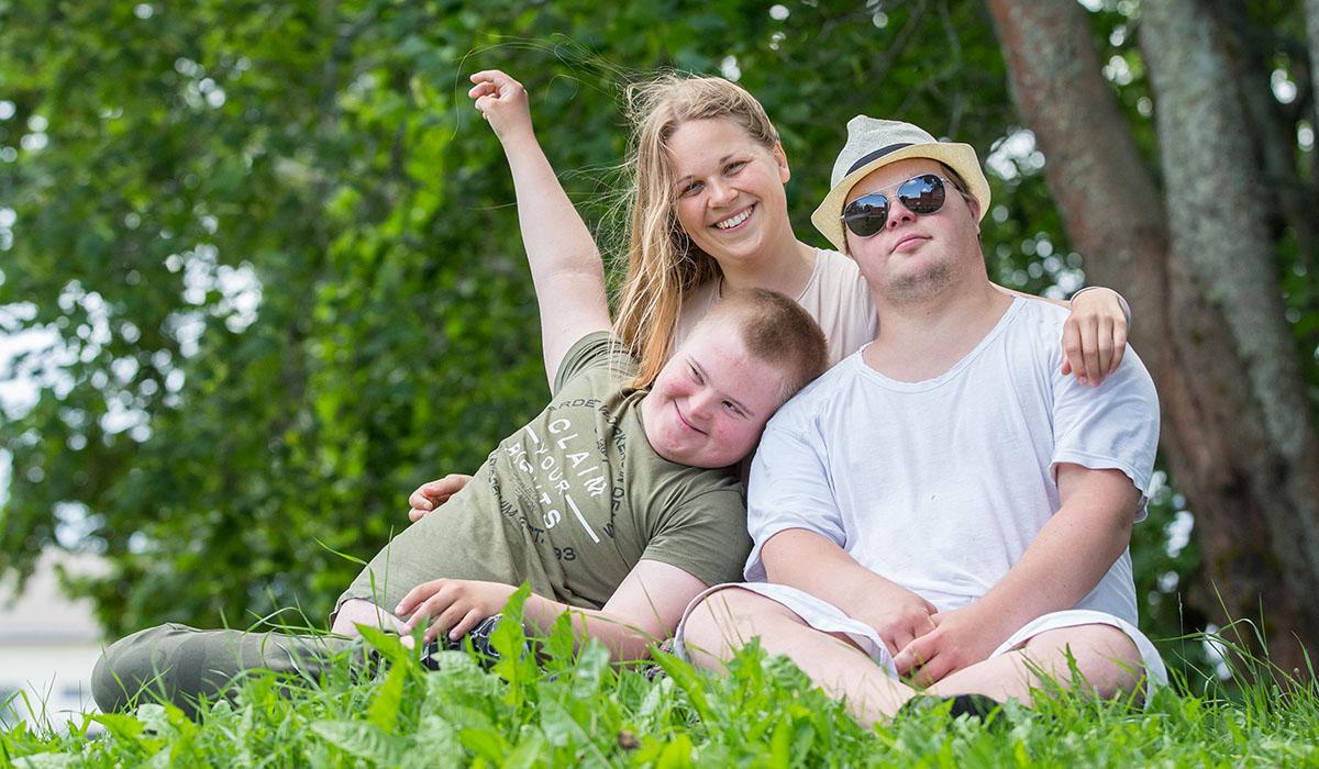 Unga killar med downssyndrom och en kvinna i somrig miljö.