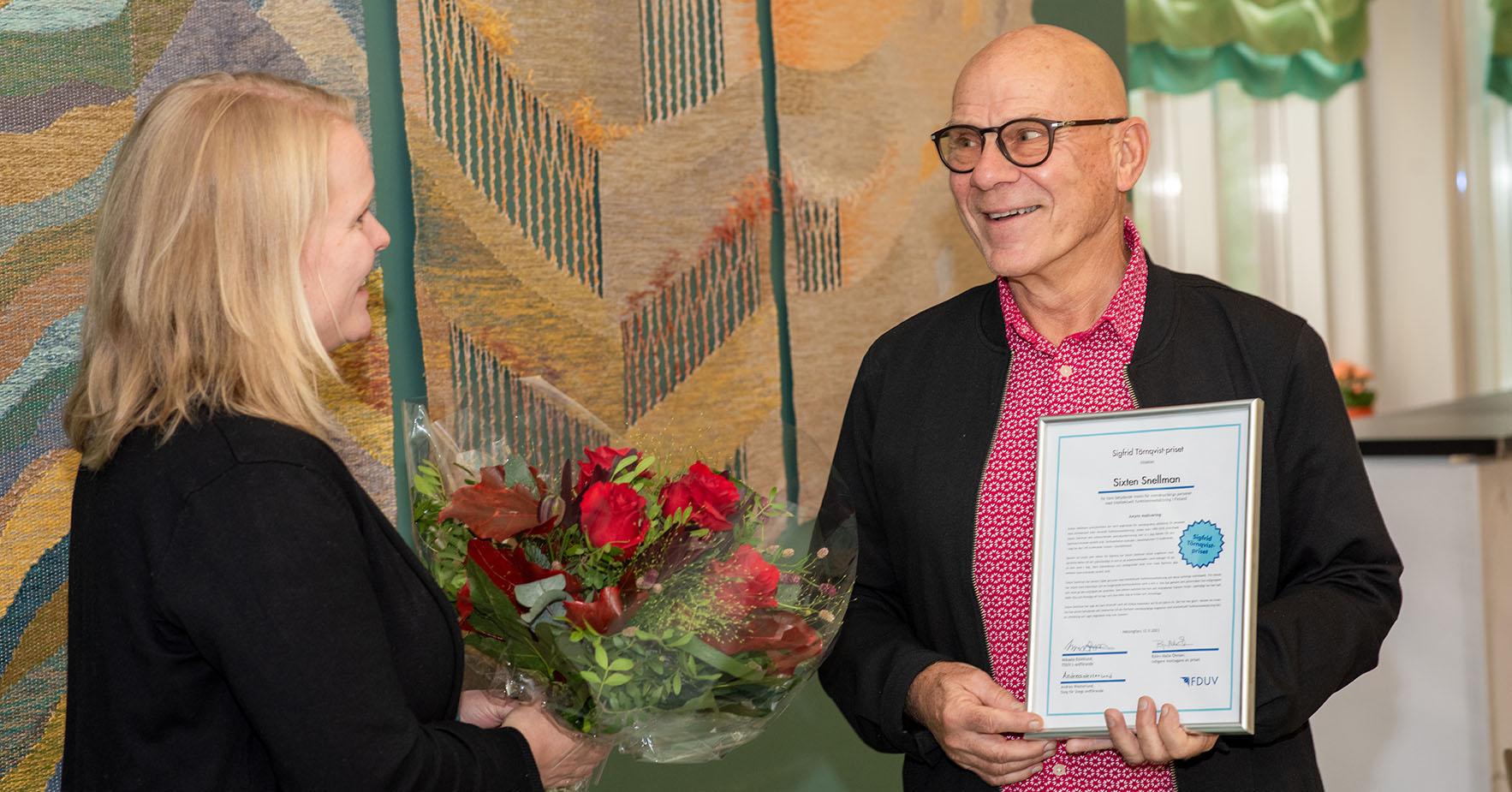 Annette Tallberg-Haahtela överräcker blommor till Sixtn Snellman som har ett diplom i handen.